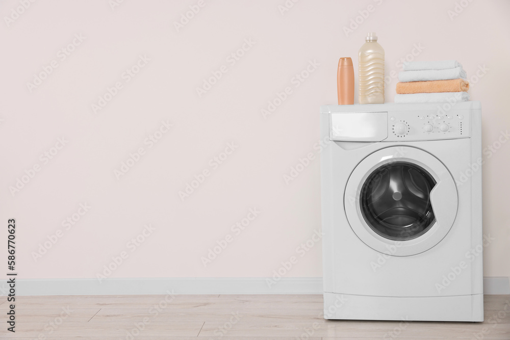 Modern washing machine, folded towels and bottles near white wall indoors. Space for text