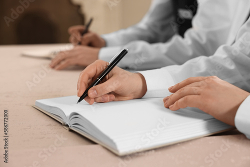 People writing notes in notebooks at table during lecture, closeup. Professional butler courses