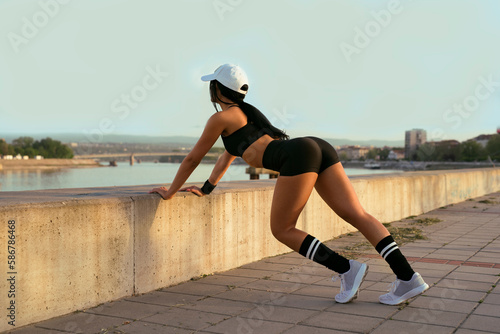 Attractive female athlete in strechy short shorts , stretching next to concrete block 