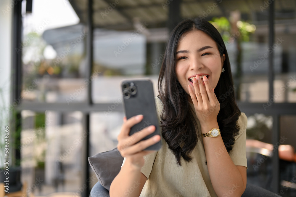 Amazed Asian female looking at her phone screen, covering her mouth, feeling excited Amazed Asian female looking at her phone screen, covering her mouth, feeling excited