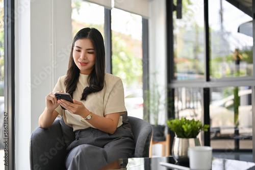 Free Download Happy Asian woman using her phone while relaxing in the coffee shop. - GFXLoad