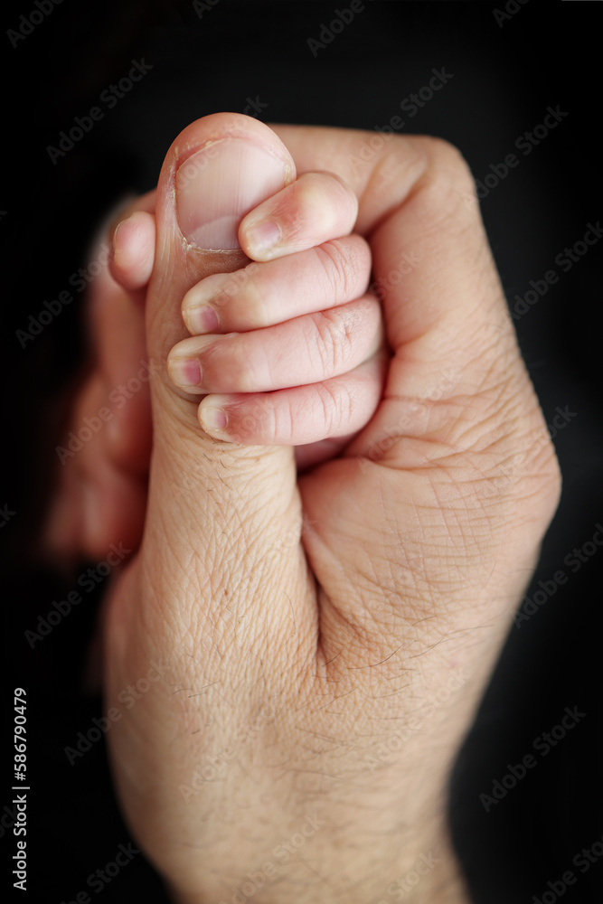 A newborn baby after birth clings tightly to the finger of the parents. Close-up of a small hand of a child and the palm of a mother and father. The concept of education, child care and healthcare. A newborn baby after birth clings tightly to the finger of the parents. Close-up of a small hand of a child and the palm of a mother and father. The concept of education, child care and healthcare.