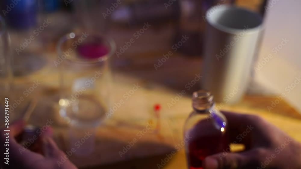 Researcher in an old laboratory with a wooden table pours a colored liquid from a bottle into a small measuring glass and then pours it into a mixing container Researcher in an old laboratory with a wooden table pours a colored liquid from a bottle into a small measuring glass and then pours it into a mixing container