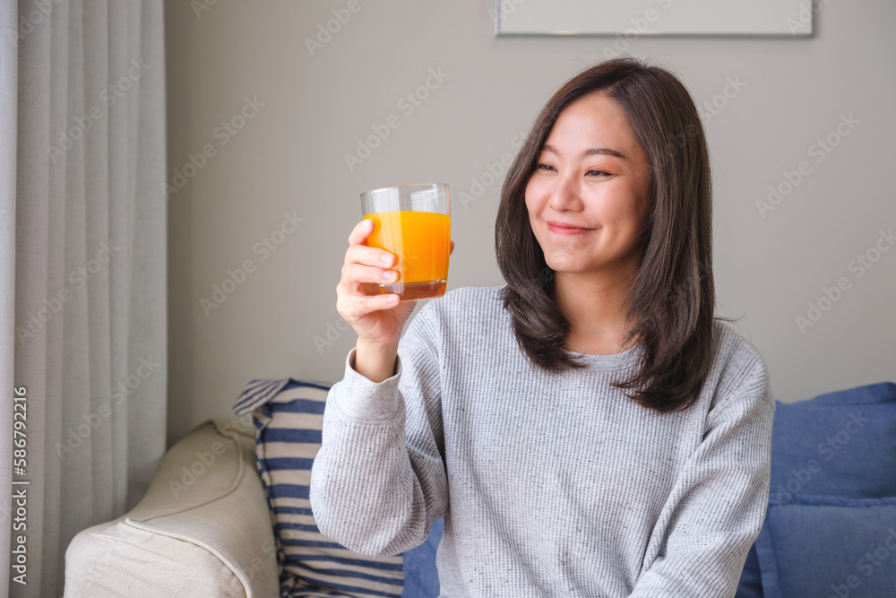 Portrait image of a young woman holding and drinking fresh orange juice at home Portrait image of a young woman holding and drinking fresh orange juice at home