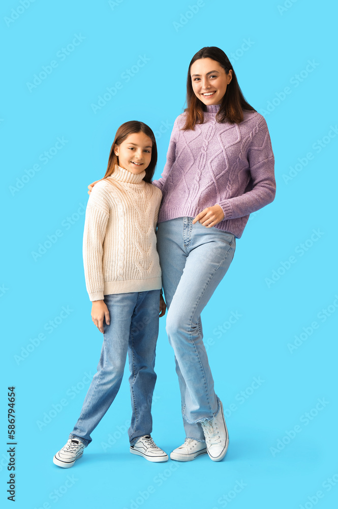 Little girl and her mother in warm sweaters on blue background Little girl and her mother in warm sweaters on blue background