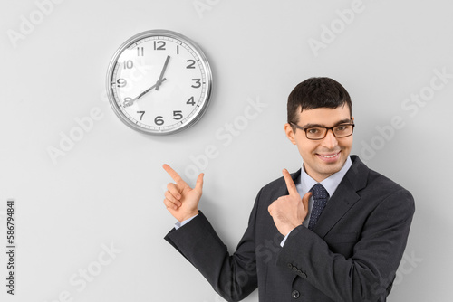 Young businessman pointing at clock on light wall