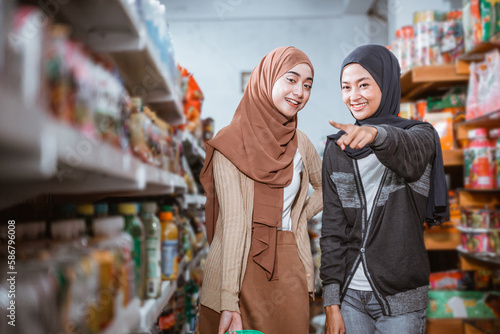 two happy muslim girls with pointing fingers while choosing shopping items in supermarket © Odua Images