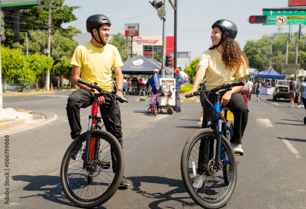 Fototapeta premium Friends man and woman cyclists using helmets riding a bike in the road in a sunny day