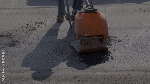 man at work filling pothole road repair street maintenance restoring asphalt with a compactor