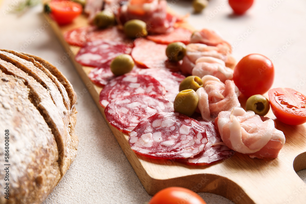 Wooden board with assortment of tasty deli meats on light background, closeup