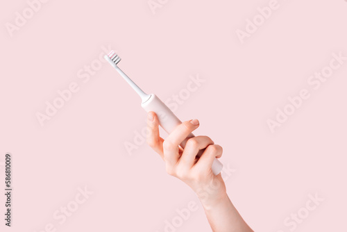 Electric toothbrush of pink color in female hand against pink background.