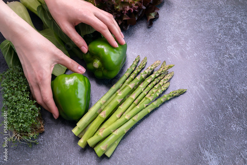 Someone Hands Hold Assortment Of Fresh Organic Home Grown Green Vegetables On Granite Table. Asparagus Plant, Bell Pepper, Bok Choy, Red Leaf Lettuce, Bittercresses. Bio food.Horizontal, copy space. photo