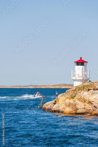 Canvas Print Children bathing in the sea by a cliff with a lighthouse