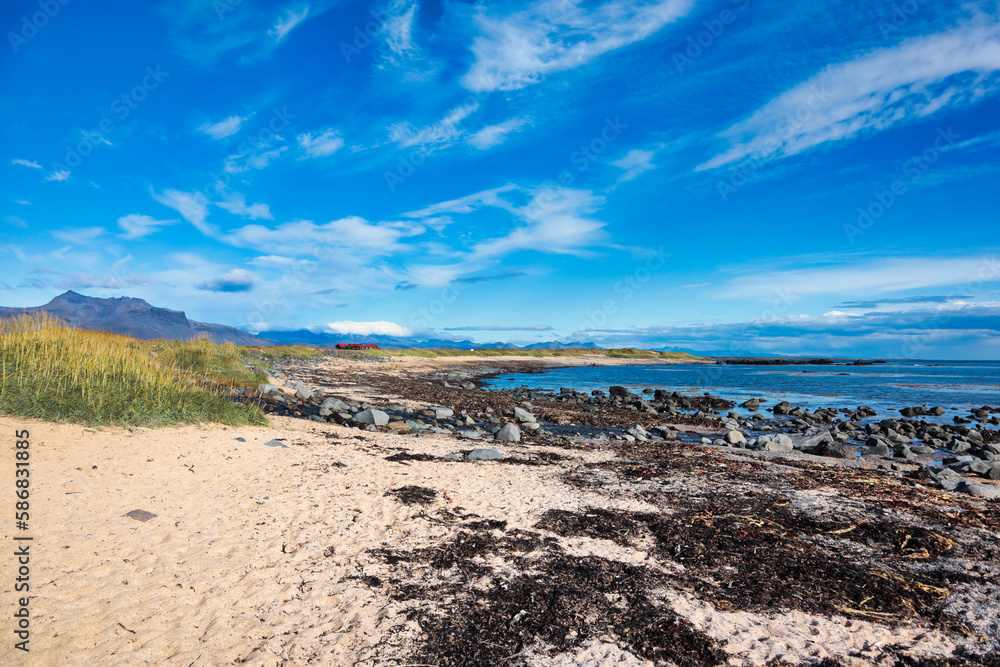 A beautiful Icelandic beach with golden sand, rocky shoreline, and distant mountains under a bright blue sky. The scene captures the serene coastal landscape of Iceland A beautiful Icelandic beach with golden sand, rocky shoreline, and distant mountains under a bright blue sky. The scene captures the serene coastal landscape of Iceland