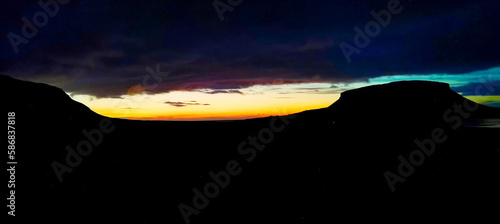 A dramatic Icelandic sunset with vibrant colors illuminating the horizon, framed by dark silhouetted mountains under a fading sky