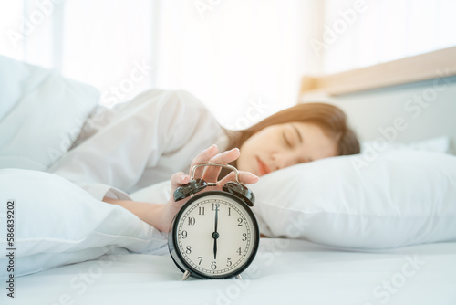 Woman sleep on the bed stopping alarm clock in the morning. young woman hand reaching for the alarm clock to turn it off.