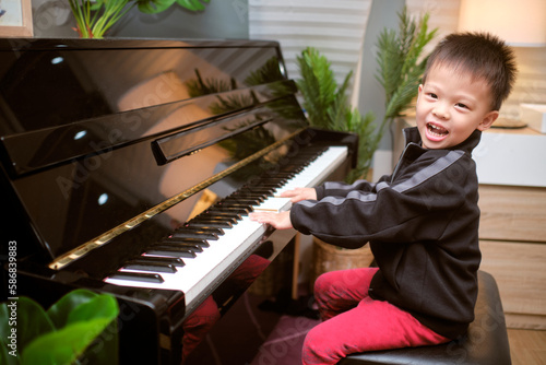 Cute happy smiling little Asian kid boy playing piano in living room at home, Preschool child having fun with learning to play music instrument, Music education concept
