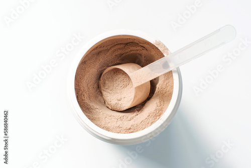 Chocolate protein powder in a scoop against plastic jar on white background.