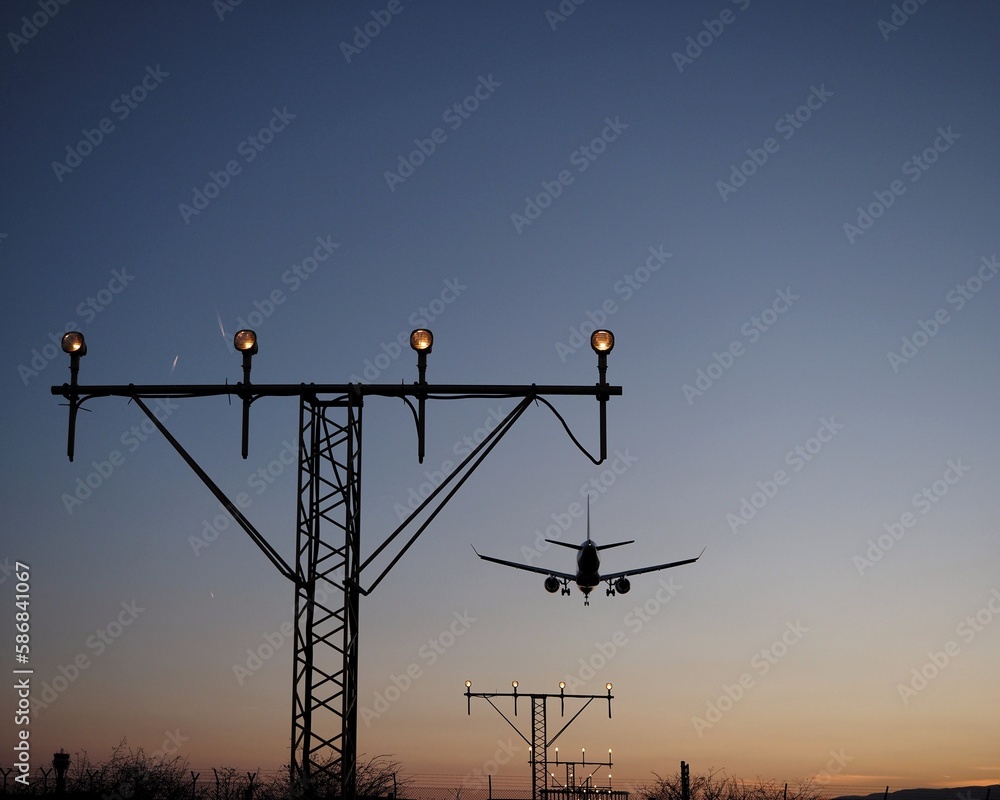 silueta de un avion aterrizando sobre las luces de aproximación de un aeropuerto al atardecer