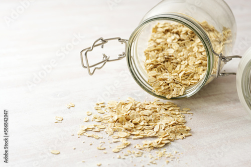 Oat flakes falling from a glass jar onto a light wooden table, healthy eating, copy space, selected focus