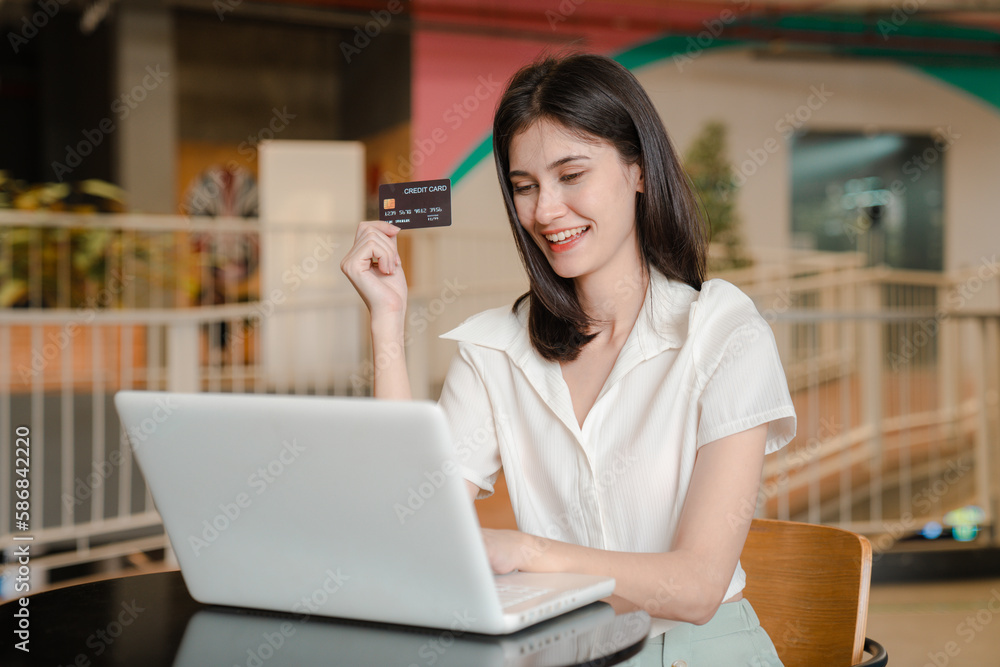 Beautiful young woman holding credit card and using laptop. online shopping concept.