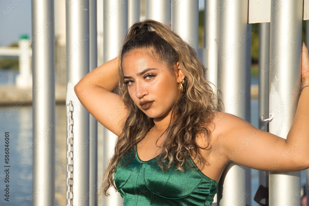 Latin and Hispanic girl, young and beautiful, with green eyes and large eyelashes, with green velvet top, clinging to a fence in a sensual and provocative attitude. Concept beauty, fashion. Latin and Hispanic girl, young and beautiful, with green eyes and large eyelashes, with green velvet top, clinging to a fence in a sensual and provocative attitude. Concept beauty, fashion.