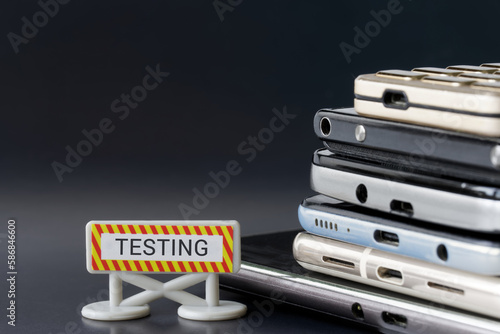 A lot of mobile phones and smartphones next to the Testing sign. Gadget testing and expertise concept. The ban on the use of a smartphone during testing or. Dark background.
