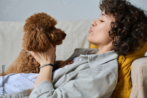 Schilderij op canvas Young woman hugging and talking to her dog while lying on sofa in her free time