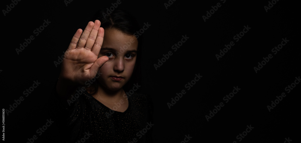 little girl with a raised hand making a stop sign gesture on a black background. Violence, harassment and child abuse prevention concept. little girl with a raised hand making a stop sign gesture on a black background. Violence, harassment and child abuse prevention concept.