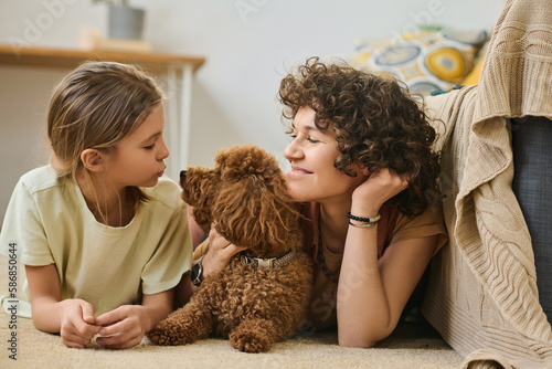 Mother and daughter lying together on the floor with their dog and enjoying leisure time