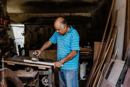latin senior man carpenter using sandpaper on a polished wood in workshop in Mexico Latin America