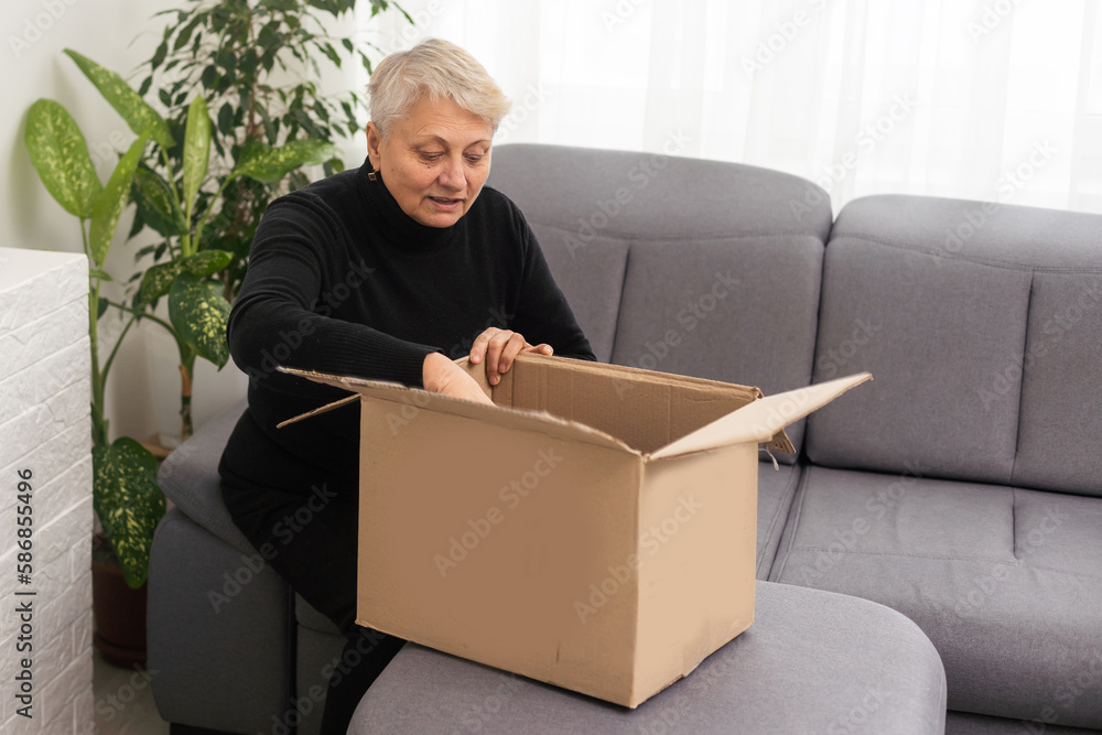 Beautiful senior woman is holding cardboard box sitting on sofa at home. Beautiful senior woman is holding cardboard box sitting on sofa at home.