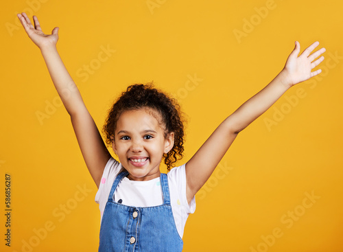 Studio, portrait and excited child with hands up and smile on face on yellow background. Young girl kid with happiness, carefree and positive attitude or happy celebration or surprise announcement