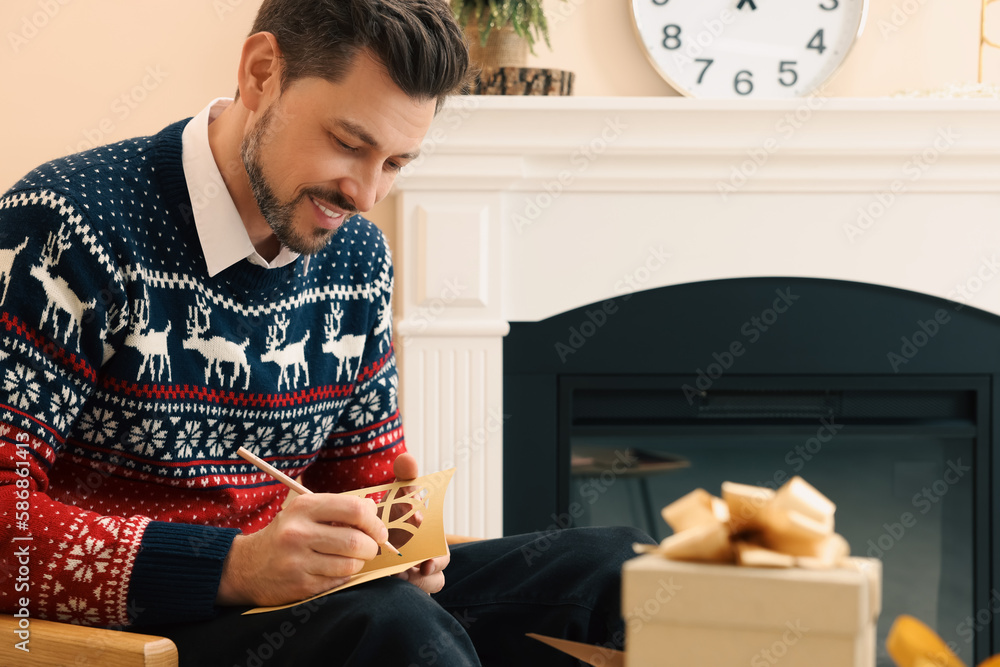 Happy man writing wishes in Christmas greeting card in living room Happy man writing wishes in Christmas greeting card in living room
