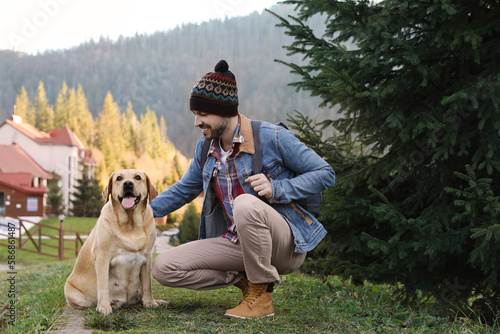 Happy man and adorable dog sitting on green grass in mountains. Traveling with pet