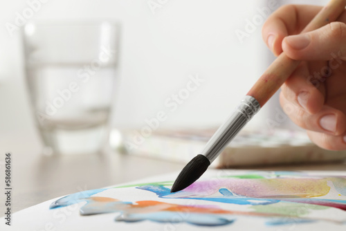 Woman painting with watercolor at wooden table indoors, closeup. Space for text