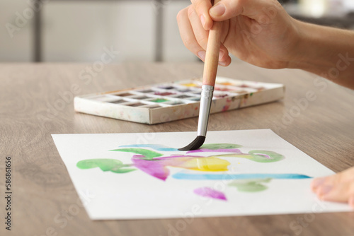 Woman painting with watercolor at wooden table, closeup