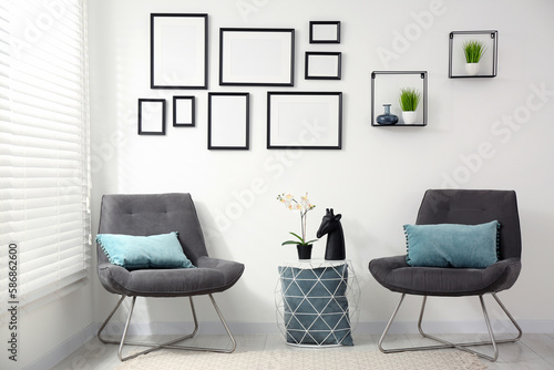 Stylish room interior with empty frames hanging on white wall and comfortable furniture