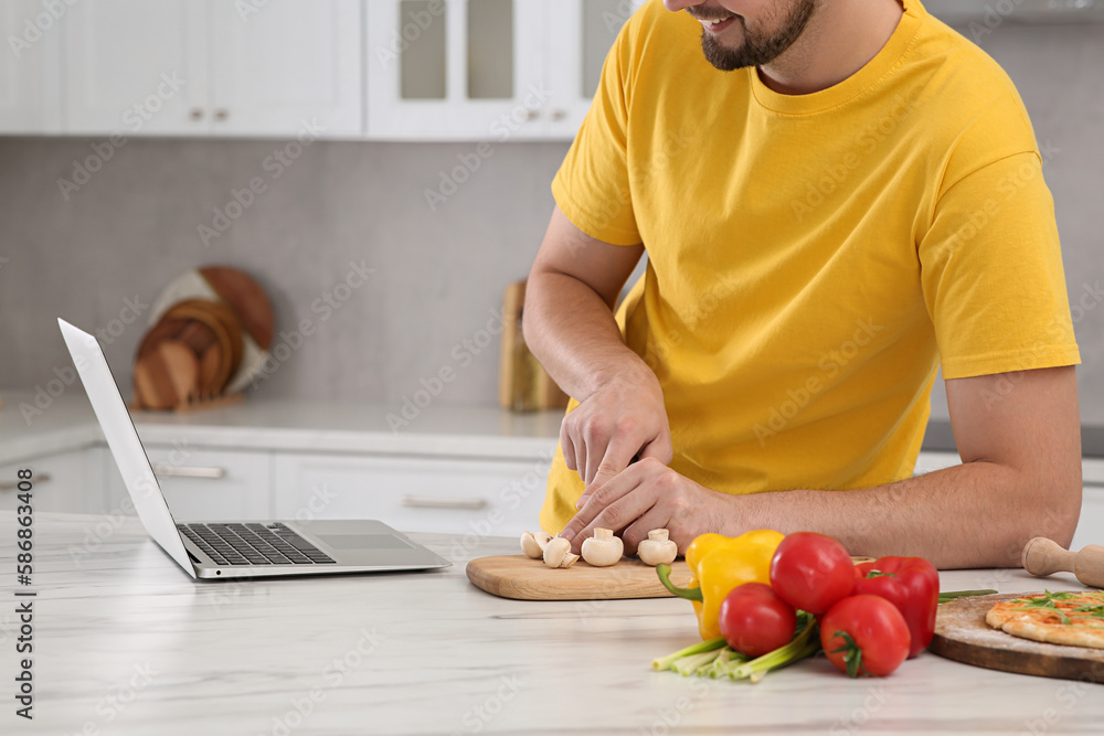 Man watching cooking online course on laptop while cutting mushrooms in kitchen, closeup. Time for hobby Man watching cooking online course on laptop while cutting mushrooms in kitchen, closeup. Time for hobby