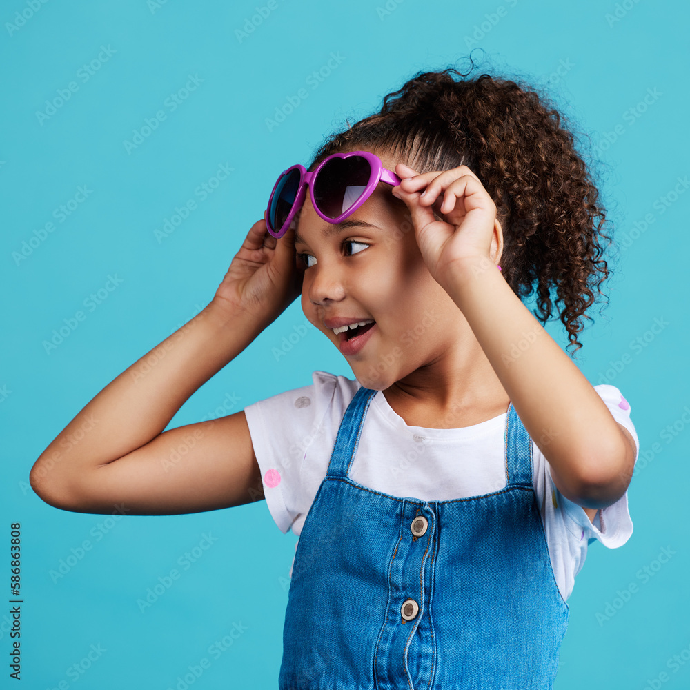Happy, smile and of a child with sunglasses in studio with positive, energy and excited face expression. Happiness, childhood and girl kid model with funky, trendy and cool glasses by blue background Happy, smile and of a child with sunglasses in studio with positive, energy and excited face expression. Happiness, childhood and girl kid model with funky, trendy and cool glasses by blue background