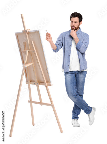 Man painting with brush against white background. Using easel to hold canvas