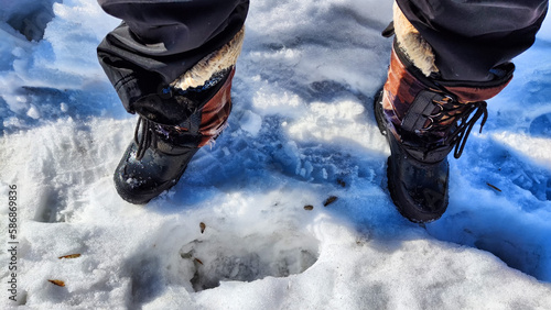 Feet of Hunter or fisherman in big warm boots on a winter day on snow. Top view. A fisherman on the ice of a river, lake, reservoir on a spring day with melting ice. Dangerous fishing