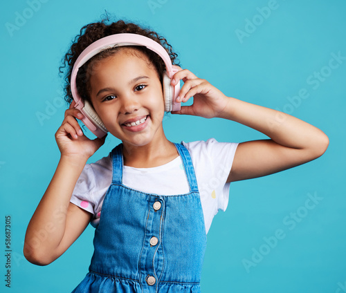 Foto Music, portrait and girl child with headphones in studio for streaming, subscription and audio on blue background