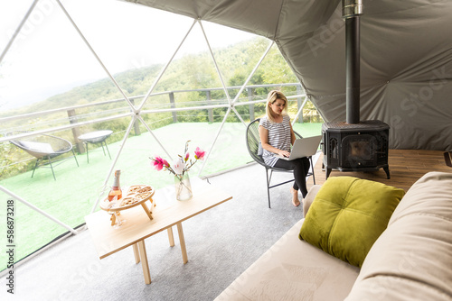 middle aged woman uses a laptop resting and spending time at Glamping house on holidays. holiday dome tent. Cozy, camping, hygge, lifestyle concept © Angelov