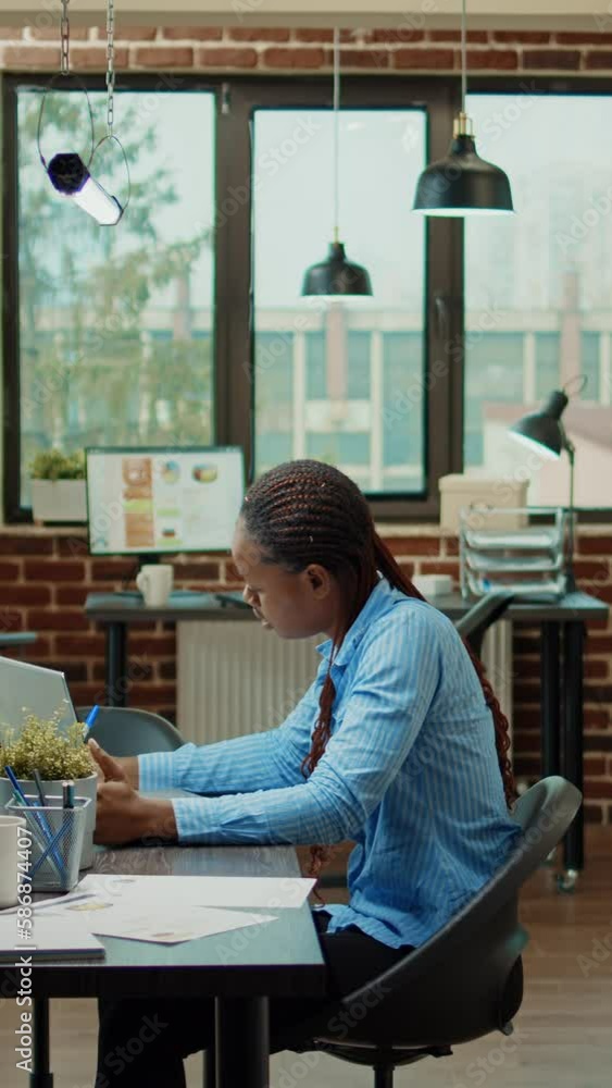 Vertical video: Startup employee writing data on laptop, planning executive briefing meeting to discuss new development vision. Female office worker examining corporate results in coworking space. Vertical video: Startup employee writing data on laptop, planning executive briefing meeting to discuss new development vision. Female office worker examining corporate results in coworking space.