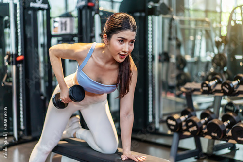 Fitness young asian woman lifting dumbbell in the gym. Morning exercise, Slim young beautiful girl warming up with weights in health club.