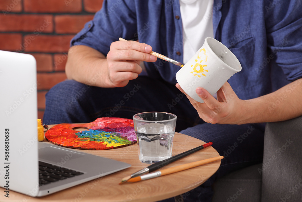Man learning to decorate cup while watching online course indoors, closeup. Time for hobby Man learning to decorate cup while watching online course indoors, closeup. Time for hobby
