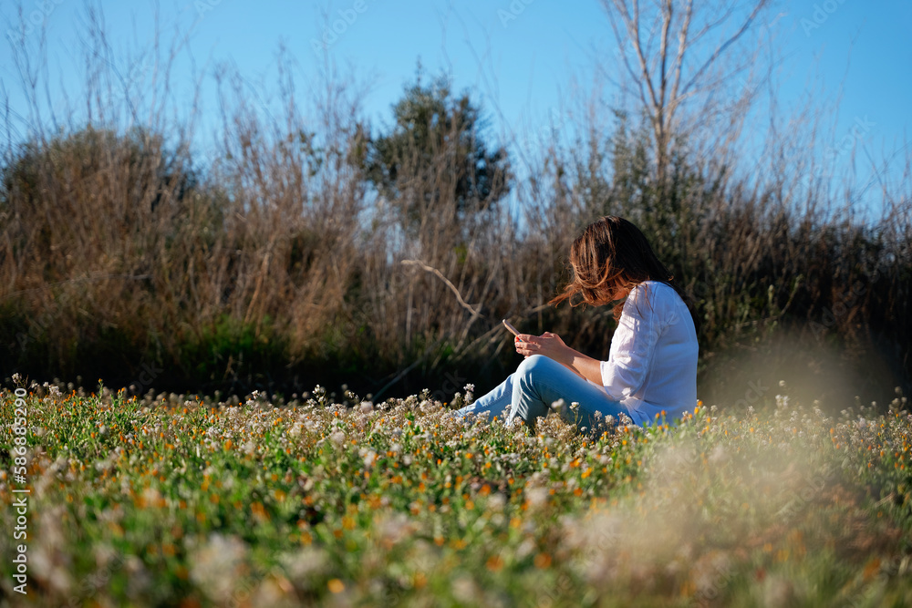 Woman checking her mobile, sitting in a field of flowers.