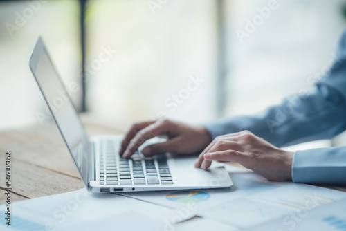 Asian businesswoman talking on phone, using laptop, looking at screen, entrepreneur manager consulting client by call, looking at computer screen, discussing