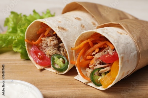 Delicious tortilla wraps with tuna on wooden board, closeup